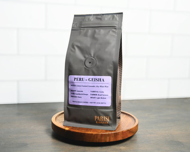 Coffee bag labeled 'Peru Geisha' by Parisi Coffee on a wooden stand with a white background