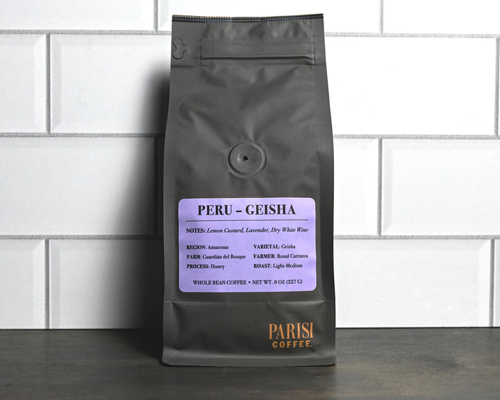 Coffee bag labeled 'Peru Geisha' by Parisi Coffee on a white tiled wall background